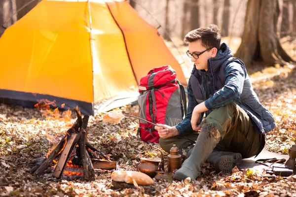 A young traveler in the forest is resting near the tent and cook