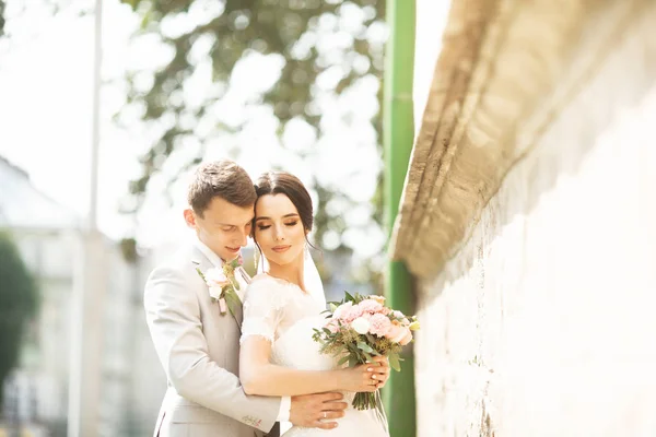 Красивая супружеская пара муж в костюме и жена в свадебном платье позирует возле кирпичной стены — стоковое фото