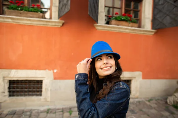 Menina sorridente bonita em um chapéu azul posa perto da velha casa vermelha — Fotografia de Stock