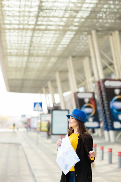 เด็กสาวสวยที่มีกระเป๋าเป้สะพายหลังอยู่หลังไหล่ของเธอถือแผนที่ในถนนใกล้สนามบิน — ภาพถ่ายสต็อก