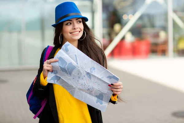 เด็กสาวที่มีกระเป๋าเป้สะพายหลังอยู่หลังไหล่ของเธอถือแผนที่ในถนนใกล้สนามบิน — ภาพถ่ายสต็อก