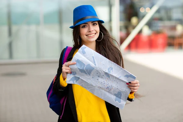Gadis muda dengan ransel di belakang bahunya memegang peta, di jalan dekat bandara — Stok Foto