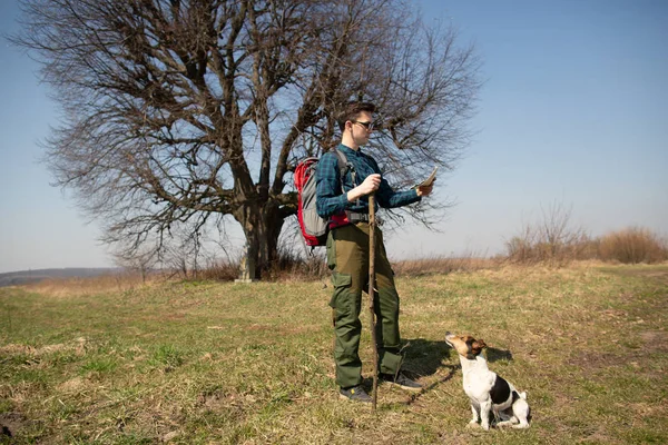 A traveler with a backpack and his dog, looking at the map and walking in the countryside