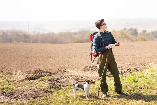 Seorang pelancong dengan ransel dan anjingnya, melihat peta dan berjalan di pedesaan — Stok Foto