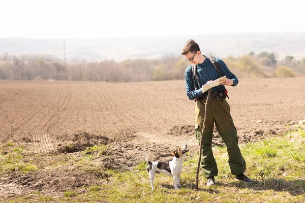 Seorang pelancong dengan ransel dan anjingnya, melihat peta dan berjalan di pedesaan — Stok Foto