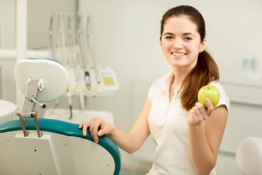 Gülümseyen ve elinde bir yeşil elma, diş bakımı ve Önleme kavramı kadın diş hekimi