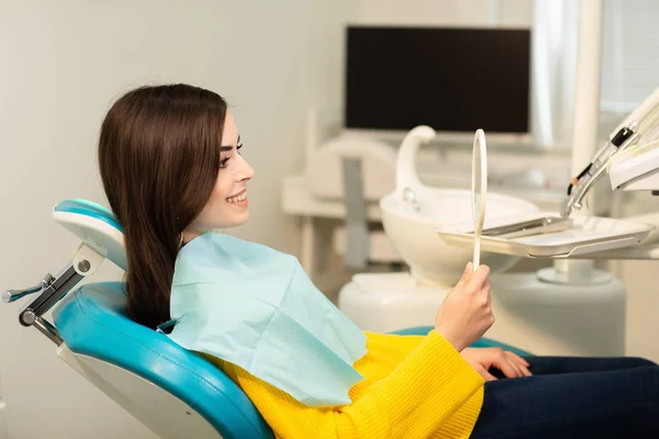 Giovane cliente donna felice guardando lo specchio con sorriso dentato allo studio dentistico — Foto Stock