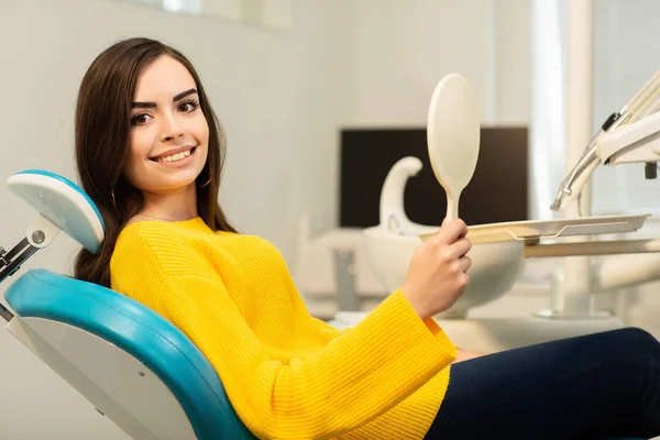 Giovane cliente donna felice guardando lo specchio con sorriso dentato allo studio dentistico — Foto Stock