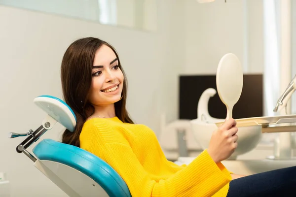 Young happy woman client looking at the mirror with toothy smile at the dental office — Stock Photo, Image