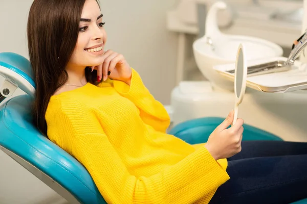 Young happy woman client looking at the mirror with toothy smile at the dental office — Stock Photo, Image