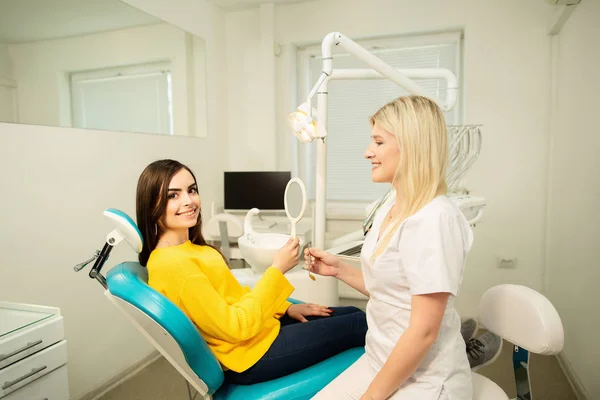 Young happy woman client looking at the mirror with toothy smile at the dental office near the doctor — Stock Photo, Image