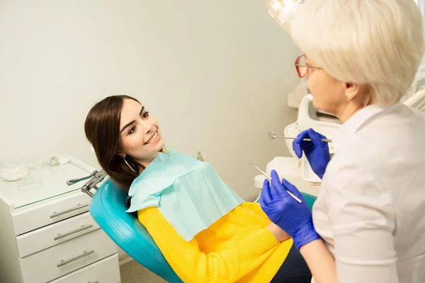 Portrait of a smiling woman, sitting at the dental chair with doctor at the dental office — Stock Photo, Image