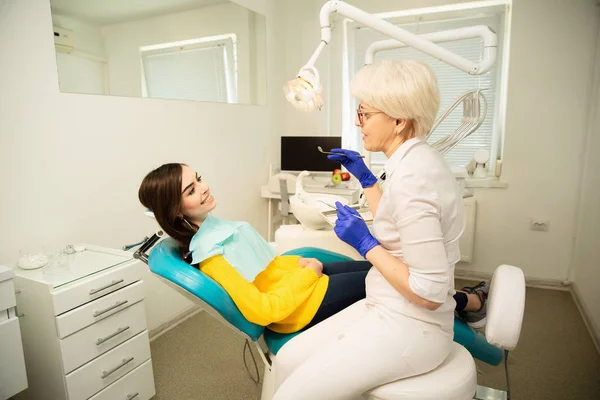 Portrait of a smiling woman, sitting at the dental chair with doctor at the dental office — Stock Photo, Image