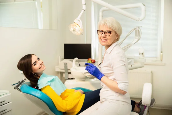 Portrait of a smiling woman, sitting at the dental chair with doctor at the dental office — Stock Photo, Image