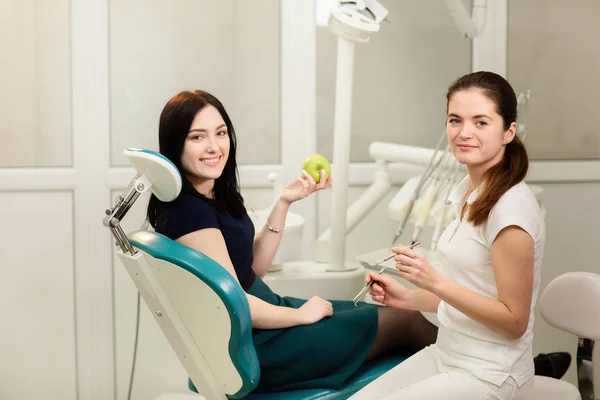 Bella paziente donna che ha un trattamento odontoiatrico nello studio del dentista. Donna sorridente tiene una mela — Foto Stock