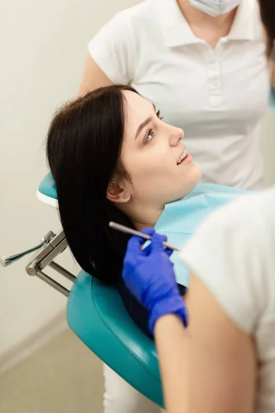歯科医の椅子に座っている若い女性患者のクローズアップ肖像画。医者は歯を調べる。歯科健康予防 — ストック写真