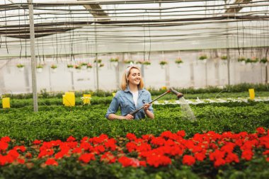 Gülümseyen genç bir kadın portakallar içinde duruyor ve bitkileri suluyor.