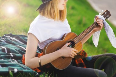 Siyah şapkalı genç ve güzel bir kadının portresi. Çimlerin üzerinde oturan ve gitar çalan kız
