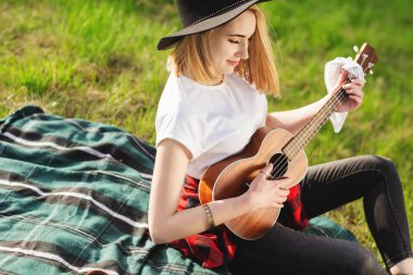 Siyah şapkalı genç ve güzel bir kadının portresi. Çimlerin üzerinde oturan ve gitar çalan kız