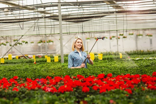 Senyum wanita muda yang cantik berdiri di orangery dan berair tanaman — Stok Foto