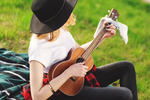 Siyah şapkalı genç ve güzel bir kadının portresi. Çimlerin üzerinde oturan ve gitar çalan kız