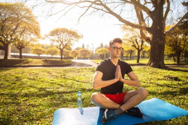Genç bir adam rahatlar ve yeşil parkta yoga yapıyor. Sağlıklı bir yaşam tarzı kavramı