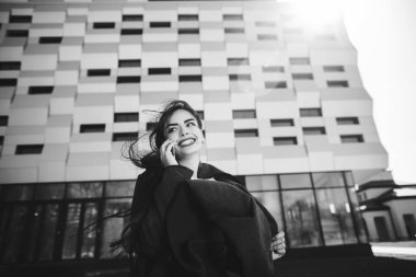 Ofis binasının yanındaki açık hava kahve molası sırasında cep telefonuyla konuşan genç bir iş kadını. İletişim konsepti