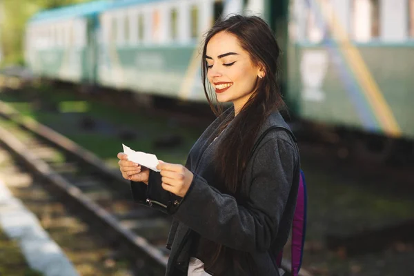 Mulher com uma mochila, perto do trem verifica seu bilhete para a plataforma da estação — Fotografia de Stock