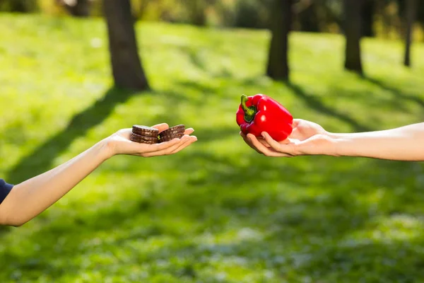 Dua tangan, perempuan dan laki-laki, memegang dan membandingkan kue dan merica merah. Latar belakang taman hijau — Stok Foto