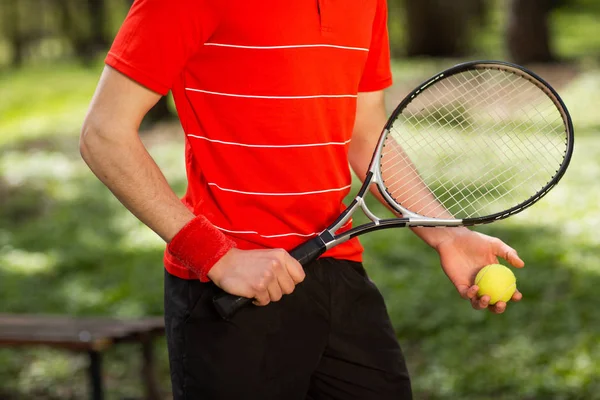 Close up de mãos masculinas segurar uma raquete de tênis e bola no fundo verde. Conceito de desporto — Fotografia de Stock