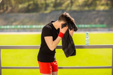 Genç sporcu dışarıda spor yaptıktan sonra terini havluyla siliyor.