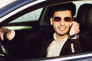 Takım elbise ve siyah Gözlük Genç bussinesman arabada telefonla konuşuyor. Bir bak. Yeni aracın test sürücü