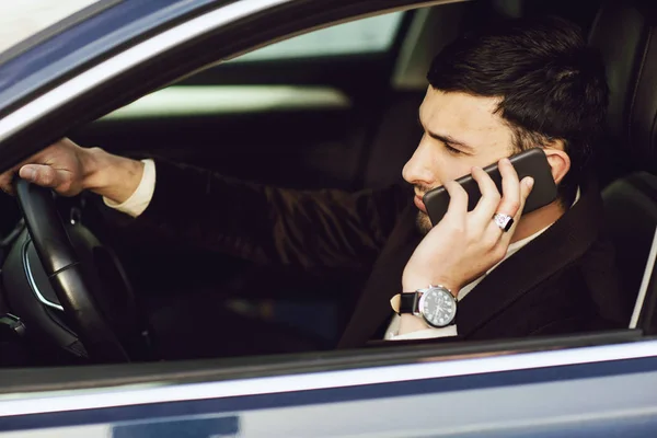 Młody biznesmen w garniturze rozmawia przez telefon w samochodzie. Biznesmeni wyglądają. Jazda próbna nowego samochodu — Zdjęcie stockowe