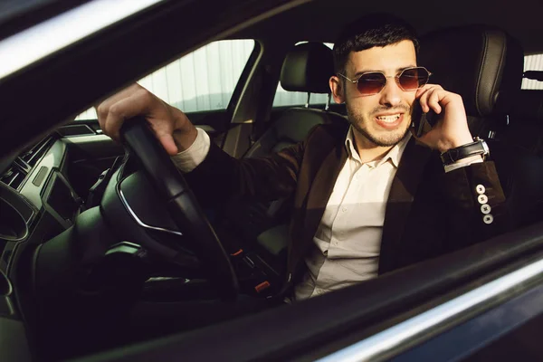 Jovem empresário de terno e óculos pretos fala por telefone em seu carro. Os negócios olham. Unidade de teste do carro novo — Fotografia de Stock