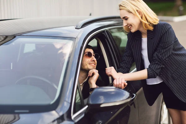Biznesmeni rozmawiają przy parkingu. Mężczyzna w okularach siedzi w samochodzie, kobieta stoi obok niego. — Zdjęcie stockowe