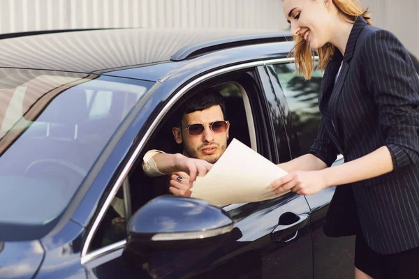 A young man rents a car. Employee of the dealer center shows documents near the car