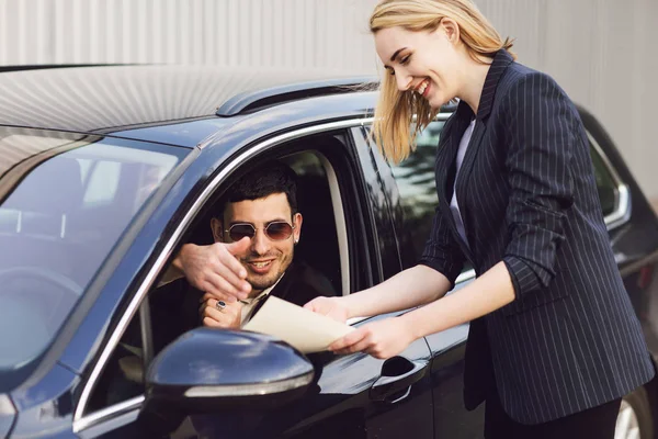 Un jeune homme loue une voiture. Employé du centre concessionnaire montre les documents près de la voiture — Photo