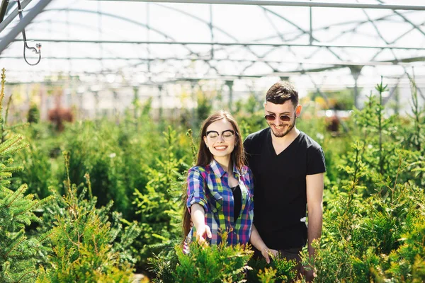 Pasangan muda, pria dan wanita, berdiri bersama di pusat kebun dan memilih tanaman untuk penghijauan rumah — Stok Foto