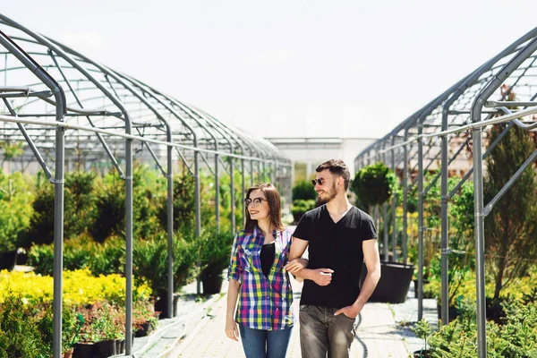 캐주얼 옷을 입은 아름다운 젊은 부부는 온실에 서있는 동안 식물을 선택하고 미소짓고 있습니다. 로열티 프리 스톡 사진