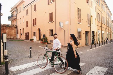 Güzel giyimli erkek ve kadın bir bisiklet ile eski şehirde yürüyorlar. Rimini, İtalya'da aşk hikayesi