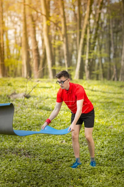 Seorang pria menebarkan tikar yoga biru di taman di rumput hijau untuk latihan dan relaksasi. Gaya hidup sehat — Stok Foto