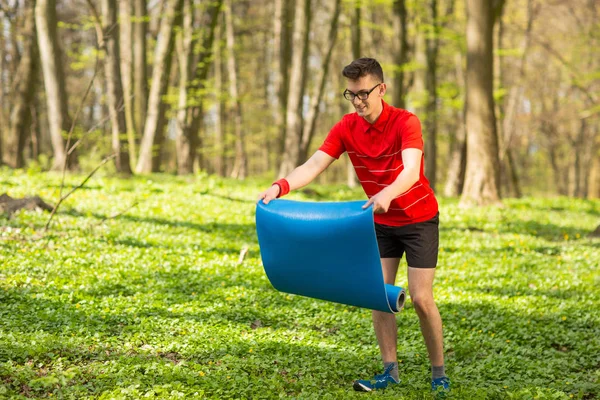 Seorang pria menebarkan tikar yoga biru di taman di rumput hijau untuk latihan dan relaksasi. Gaya hidup sehat — Stok Foto