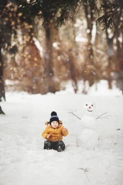 Açık havada bir kardan adamla oynayan güzel bir çocuk.