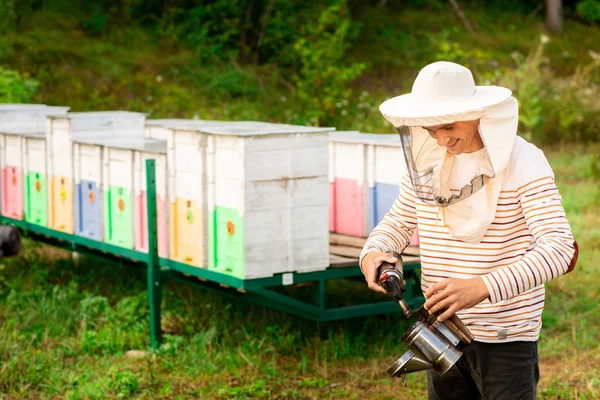 Ein Imker mit Schutzkappe bereitet aus einem Bienenstock im Bienenhaus ein Werkzeug zum Räuchern der Bienen zu. Rauch für Bienen, Geräte für die Imkerei — Stockfoto