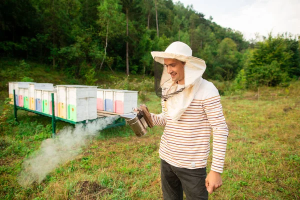 Peternak lebah dalam topi pelindung menyiapkan alat untuk merokok lebah dari sarang lebah di peternakan lebah. Asap untuk lebah, peralatan di peternakan lebah — Stok Foto