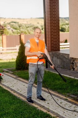 Turuncu yelekli bir adam evin yakınındaki bahçesinde kiremit temizler. Yüksek basınçlı temizlik