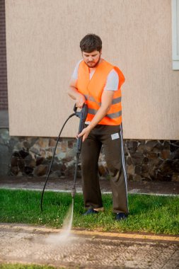 Turuncu yelekli bir adam evin yakınındaki bahçesinde kiremit temizler. Yüksek basınçlı temizlik