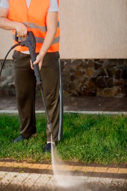Turuncu yelekli bir adam bahçesindeki çimenleri temizler. Yüksek basınçlı temizlik