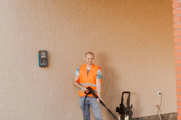 Seorang pria pekerja dengan rompi oranye membersihkan genteng di halaman dekat rumah. Pembersihan tekanan tinggi — Stok Foto