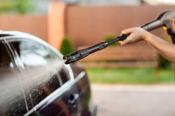 Seorang pria mencuci mobilnya dengan kepala besar air dari karcher di udara terbuka. Tutup foto — Stok Foto